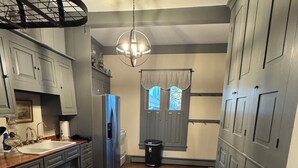A narrow kitchen with wooden flooring, grey cabinets, a built-in refrigerator, and a hanging light fixture. - Superb 4-bedroom historical house in Fredericktown (Fredericktown)
