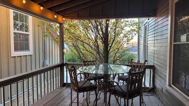 A covered outdoor seating area with a glass table and metal chairs, surrounded by wooden railings and a view of trees and a house. - Superb 4-bedroom historical house in Fredericktown (Fredericktown)