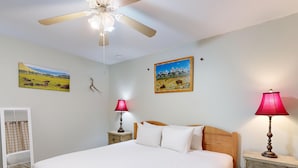 Een slaapkamer met een groot bed, twee nachtkastjes met lampen, een plafondventilator en twee landschapsprenten aan de muur.