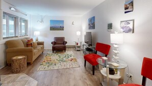 Een woonkamer met een bank, fauteuils, een glazen salontafel en een vloerkleed.