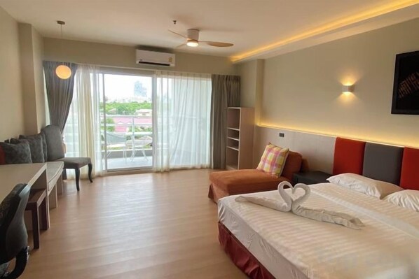 A hotel room with a bed, a desk, a chair, a sofa, and a balcony with curtains. - View Talay Studio (Pattaya)