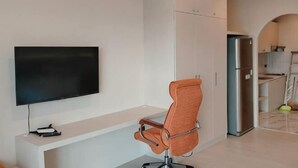 A modern living room with a flat-screen TV, a swivel chair, and a built-in kitchen area. - View Talay Studio (Pattaya)