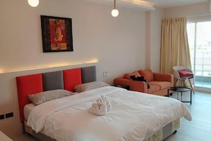 A hotel room with a bed, a sofa, a chair, a window with curtains, and a framed picture on the wall. - View Talay Studio (Pattaya)