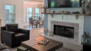 Un salon avec une cheminée, un téléviseur fixé au-dessus, et un coin repas à l’arrière-plan.