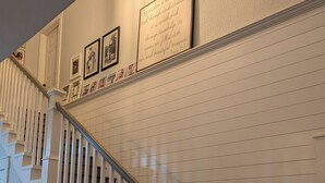 Un escalier avec des rampes blanches et des marches sombres, menant à un palier orné de citations et de tableaux encadrés.
