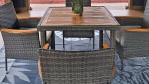 En udendørs terrasse med et bord og stole, udsigt til et træhegn og et hus i baggrunden.