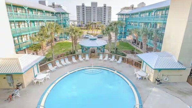 Une piscine dotée de chaises longues et d ’un kiosque, le tout entouré d’immeubles avec des balcons.