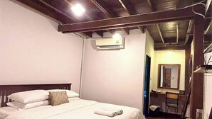 Ein Schlafzimmer mit einem Bett, einem Holzkopfteil, einer Klimaanlage, einem Spiegel und einem Schreibtisch mit Stuhl.