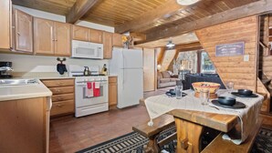 A rustic kitchen with wooden cabinets, a microwave, a stove, and a dining area with a table set for four. - New Listing! In Town, Ski-In, Ski-Out! "Claim Jumper A-Frame 6" Pet Friendly, (Red River)