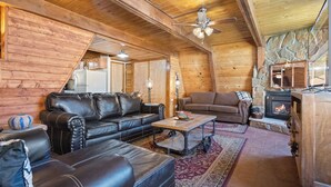 A log cabin interior with a fireplace, leather sofas, a dining table, and a ceiling fan. - New Listing! In Town, Ski-In, Ski-Out! "Claim Jumper A-Frame 6" Pet Friendly, (Red River)
