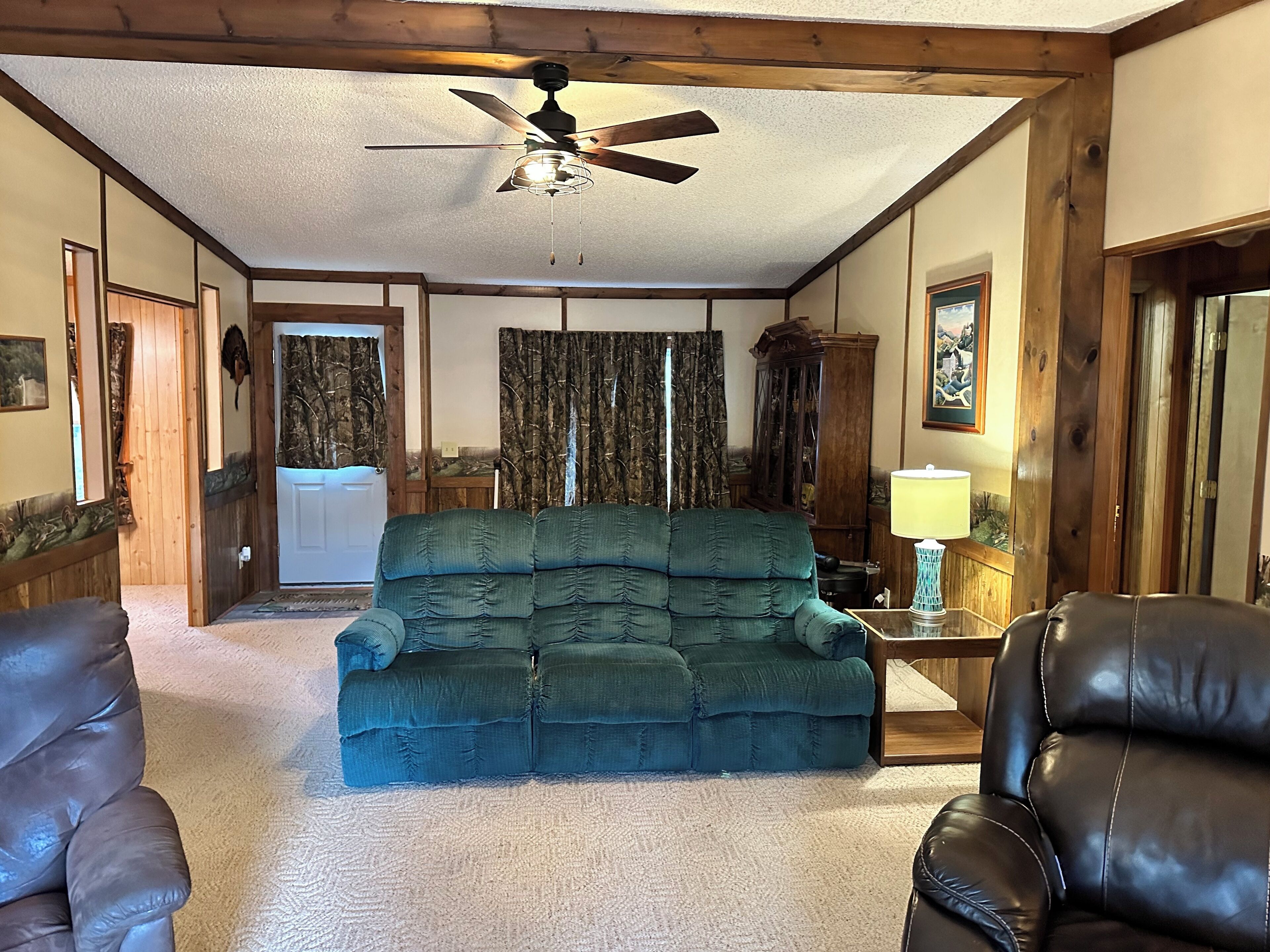 A living room with a green sofa, two leather chairs, a ceiling fan, and a wooden cabinet.