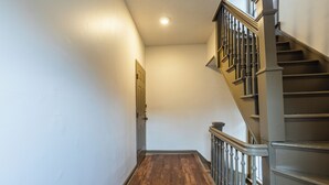Un pasillo con piso de madera, una puerta y una escalera con barandilla.