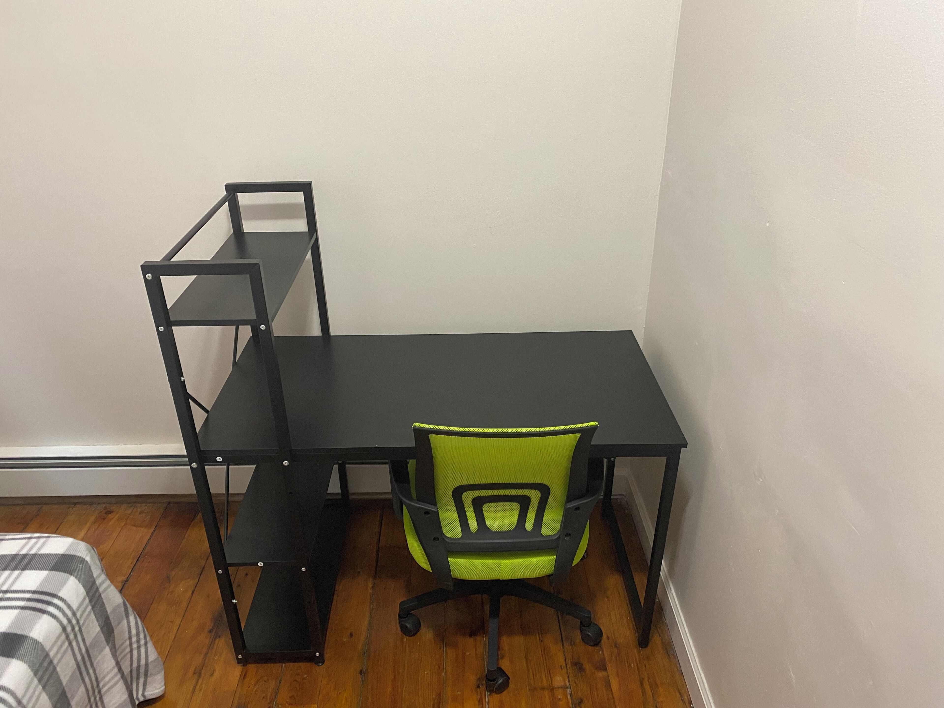 Een compact, netjes ingerichte werkplek met een zwart bureau, een groene stoel en een metalen schapunit.