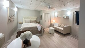 A bedroom with a bed, a sofa, a small table with a vase, a ceiling fan, and a door with a mirror. - Cozy Studio Retreat W/ Pool Near Charlotte Airport (Gastonia)