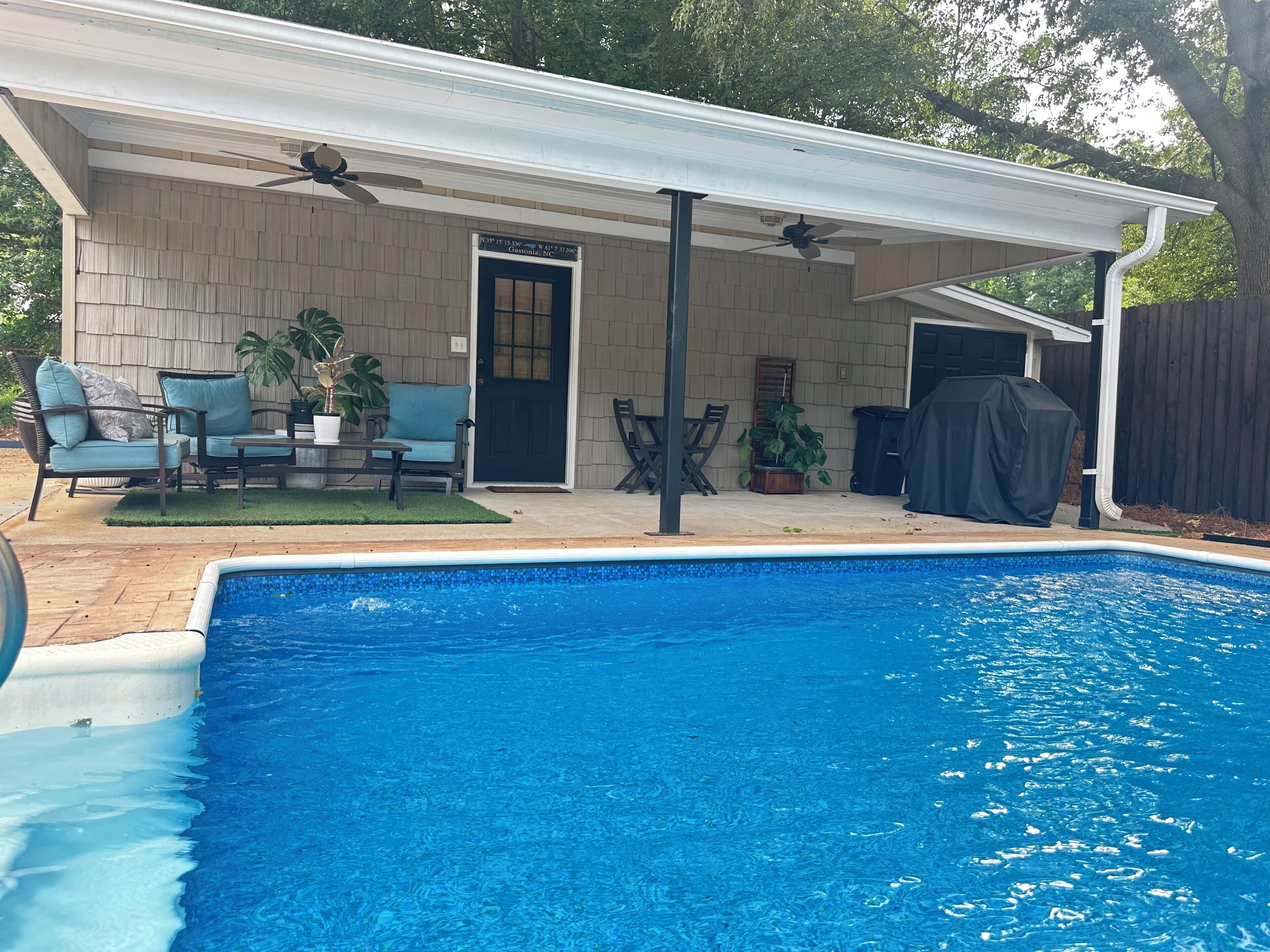 Un jardin avec une piscine, des meubles de jardin et un espace salon abrité.