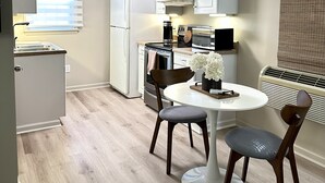 A compact kitchen with white cabinets, a refrigerator, a microwave, and a stove. There is a dining table with two chairs and a vase of flowers. - Cozy Studio Retreat W/ Pool Near Charlotte Airport (Gastonia)