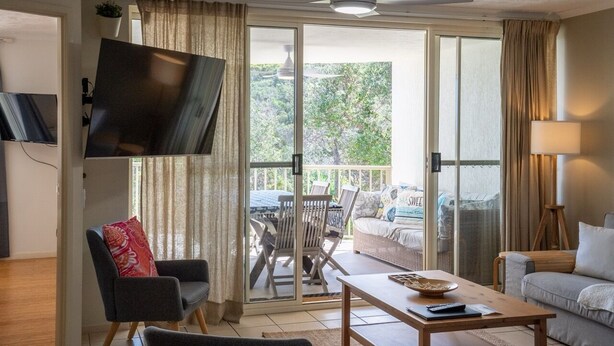 Ett vardagsrum med en platt-TV, en soffa, ett soffbord och en balkong med utemöbler.