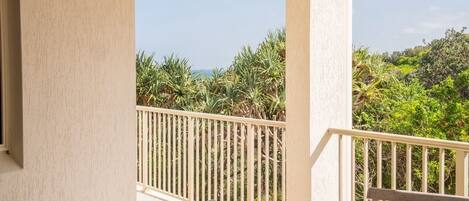A balcony with a table and chairs, overlooking a lush landscape with palm trees and a view of the sea.