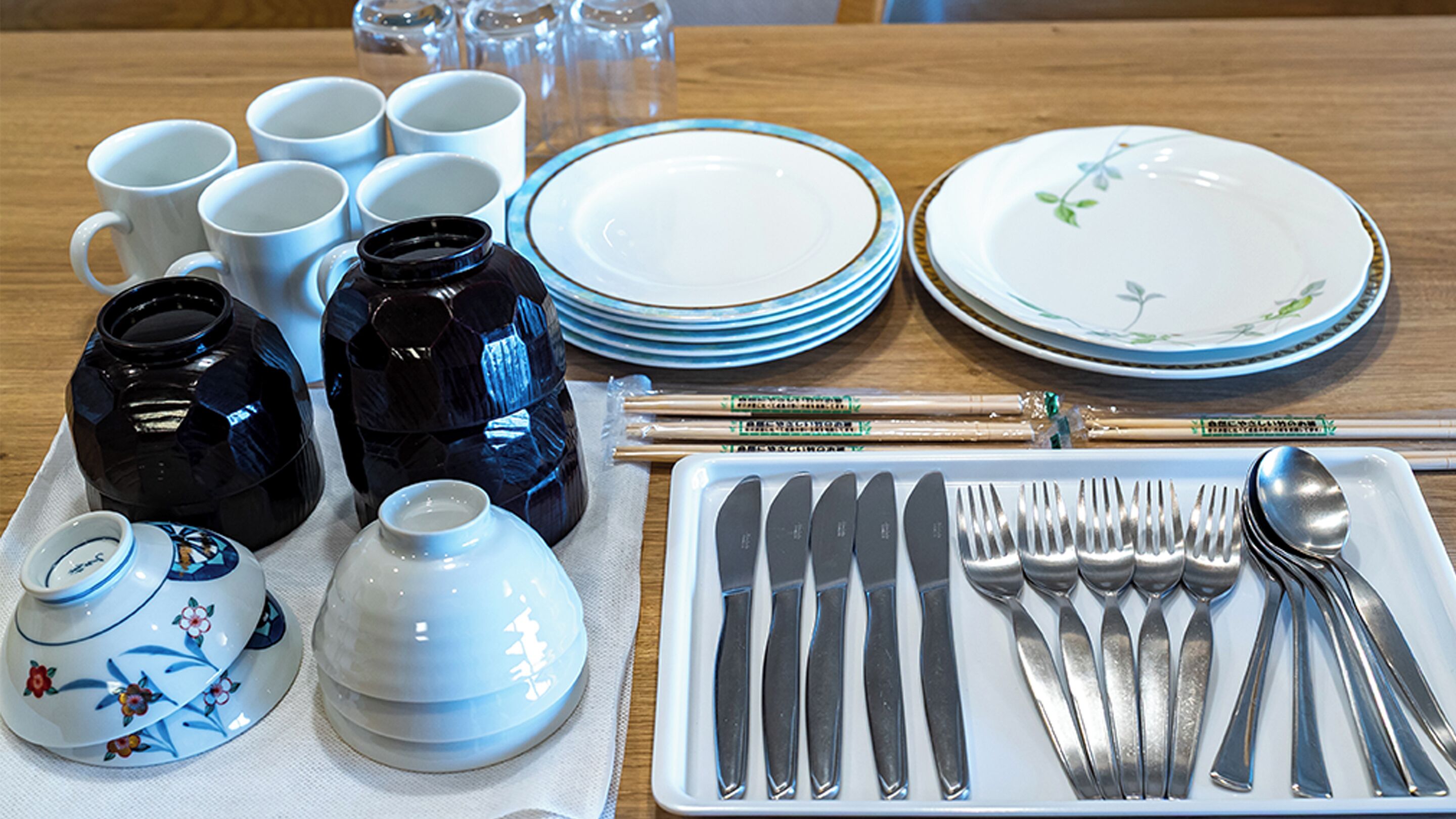 A dining table set with plates, cups, bowls, chopsticks, and cutlery.