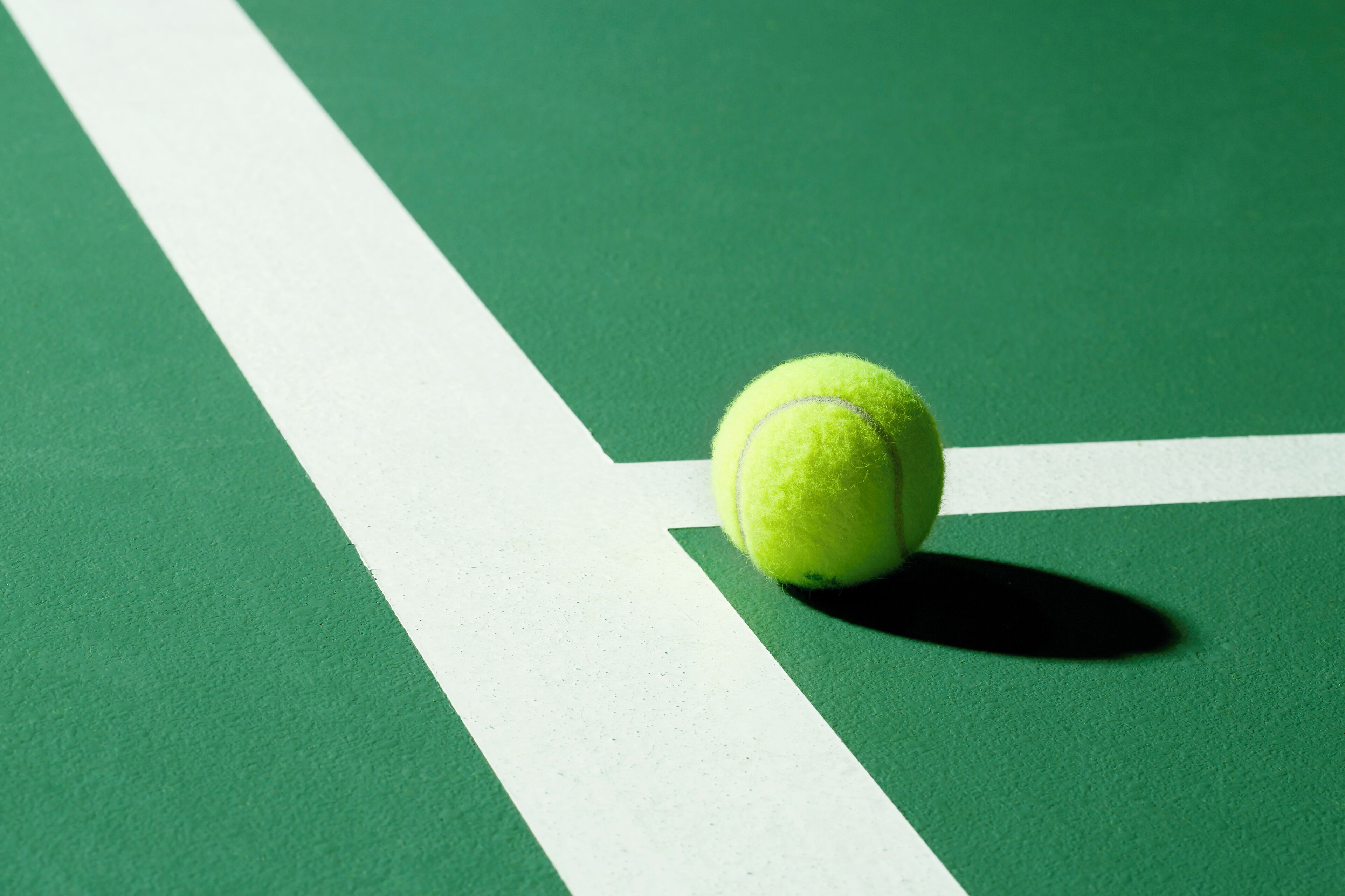 A tennis ball on a green court with white lines.