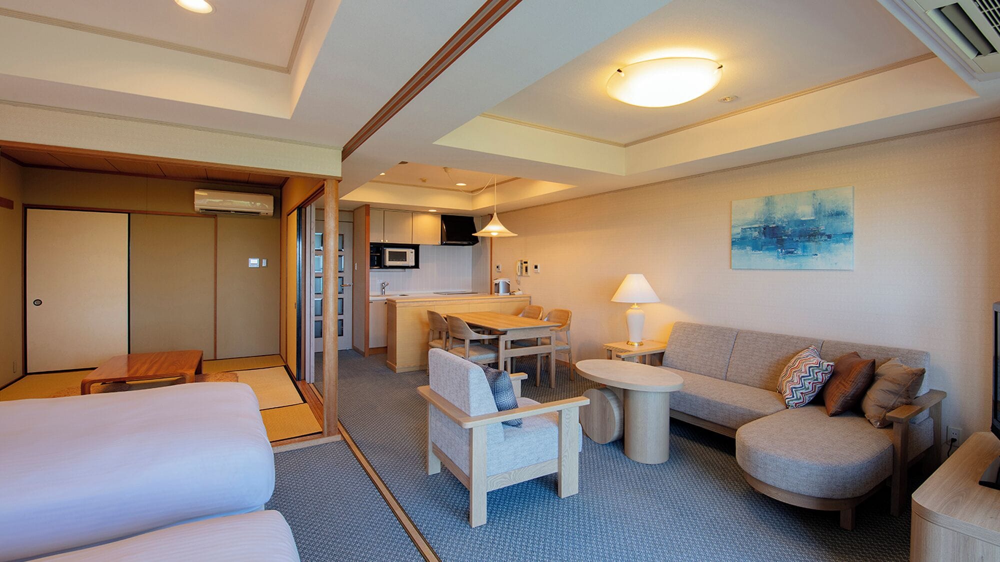 Una habitación de hotel compacta con kitchenette, un sofá, una pequeña mesa de comedor y un área tradicional con tatami japonés.