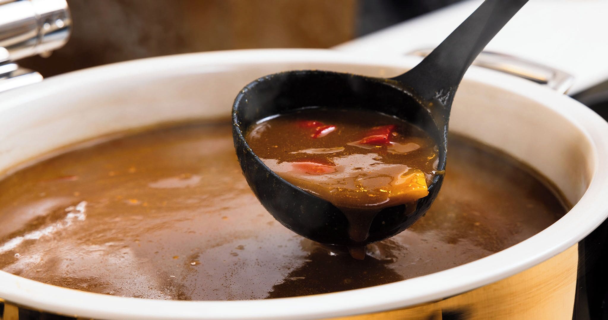 A soup in a black ladle with visible ingredients like red peppers and carrots.