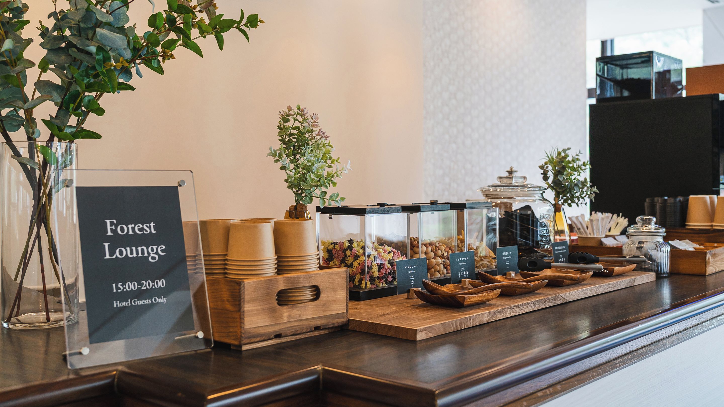 Un espace détente de l’hôtel, avec un panneau indiquant les heures d’ouverture du bar « Forest Lounge » et divers distributeurs de nourriture et de boissons.