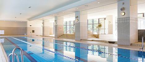 A large indoor swimming pool with clear lanes, a lifeguard chair, and a clock on the wall.