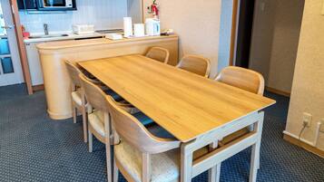 Habitación de hotel con una mesa de comedor de madera, cuatro sillas, un microondas, un lavamanos y un extintor.