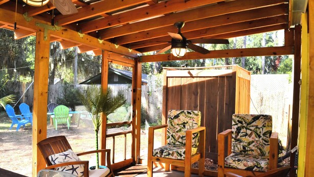 Un espacio de estar al aire libre techado con mobiliario de madera y un ventilador de techo.
