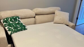 Una cama con un colchón blanco texturizado, una almohada estampada con hojas verdes y un cabecero color beige.