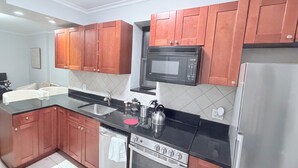 Una cocina moderna con armarios de madera, encimera negra, electrodomésticos de acero inoxidable y salpicadero de azulejos.