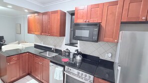 Eine moderne Küche mit Holzschränken, einer schwarzen Arbeitsplatte, Edelstahlgeräten und einer gefliesten Spritzschutzwand.