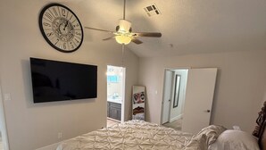 Un dormitorio con cama, ventilador de techo, televisión montada en la pared y un reloj.