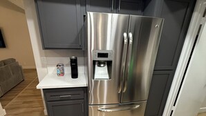 Una cocina moderna con un refrigerador de acero inoxidable, un dispensador de agua integrado y una pequeña encimera con una cafetera.