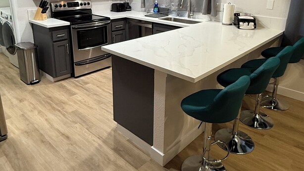 Una cocina moderna con armarios oscuros, electrodomésticos de acero inoxidable, encimera de mármol y taburetes de bar color turquesa.