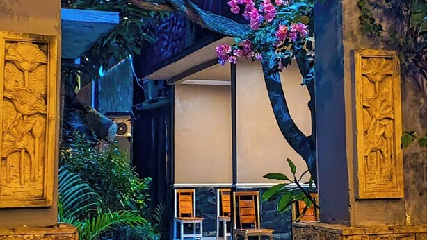A pathway leading to a seating area with chairs and a table, surrounded by stone walls and greenery. - Ayu Homestay (Kuta)