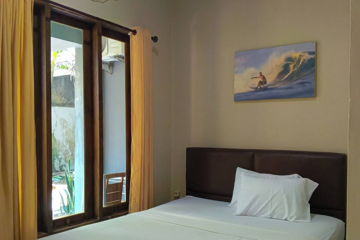 Una habitación de hotel con cama, cortinas, un cuadro y un equipo de aire acondicionado.