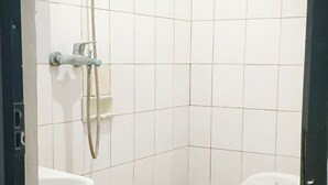 A small bathroom with white tiles, a shower, a sink, and a toilet. - Ayu Homestay (Kuta)