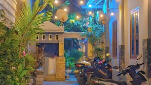 A narrow stone-paved alleyway with a row of parked scooters on one side and a small outdoor seating area with a table and chairs. - Ayu Homestay (Kuta)