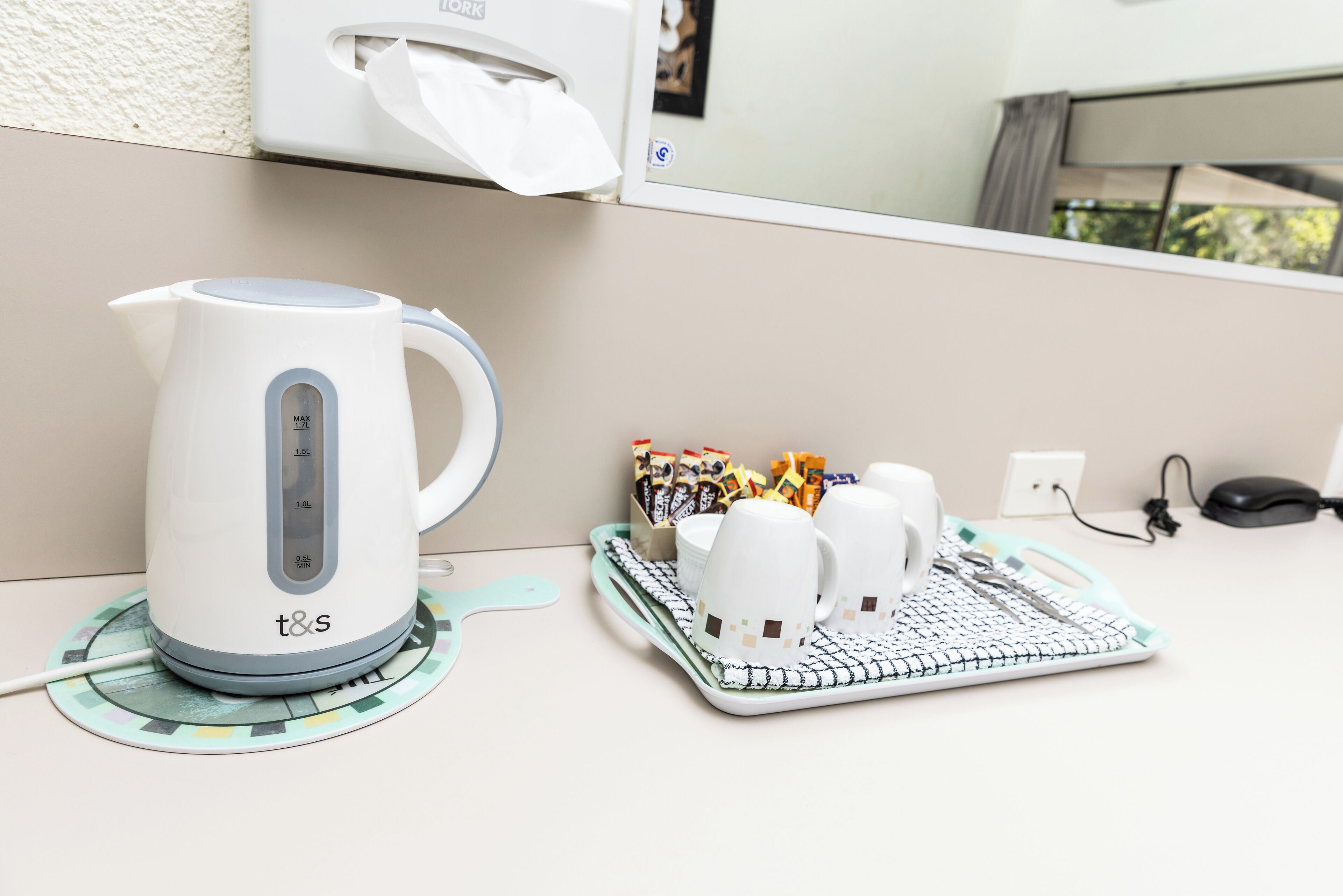 Ein weißes Wasserkocher mit digitaler Anzeige, ein Tablett mit Tassen und Teebeuteln und eine Steckdose auf einer weißen Arbeitsplatte.