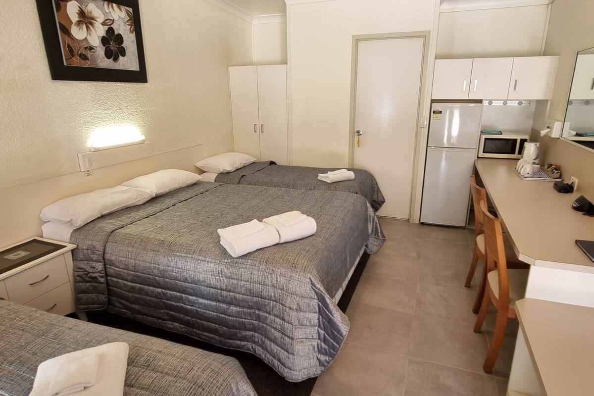 A hotel room with two beds, a desk, a chair, a refrigerator, a microwave, and a small kitchenette.