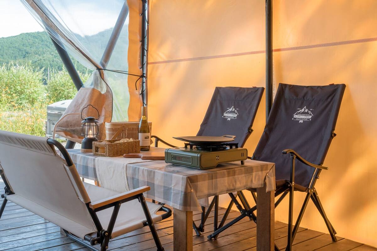 Een overdekte eethoek buiten met een tafel voor twee personen, een draagbare grill en een lantaarn.