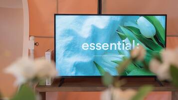 Un televisor mostrando la palabra “essential:” sobre un fondo de hojas verdes y cielo azul.
