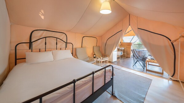 Een knus slaapkamer in tentstijl met een groot bed, twee stoelen en een klein tafeltje.