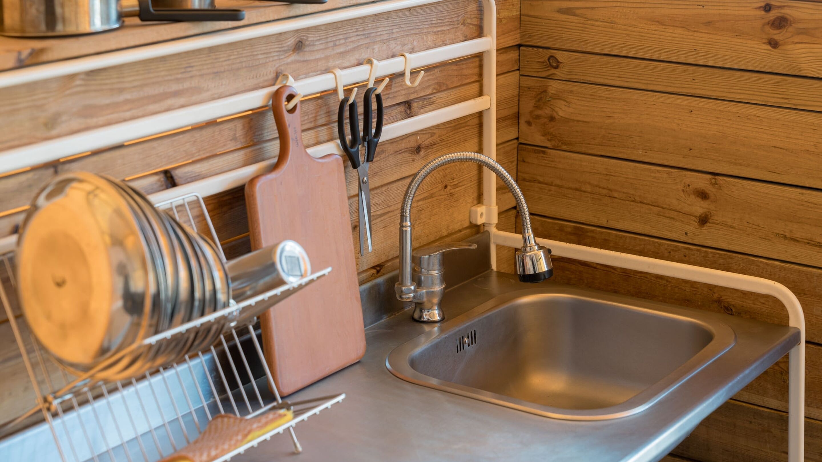 Een keuken met een roestvrijstalen spoelbak, houten wandbekleding en een afwasschaal met keukengerei.