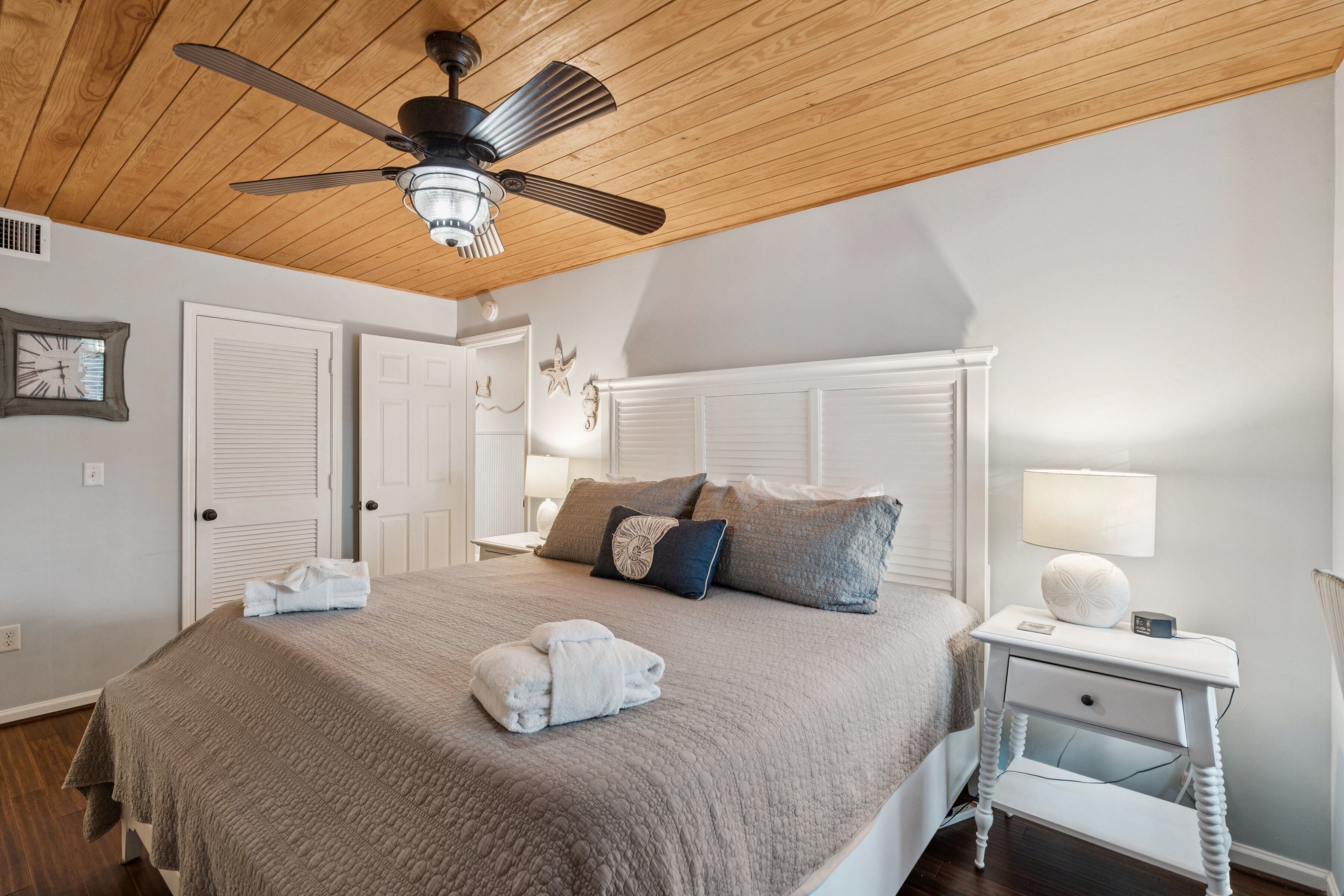 Un dormitorio con cama, mesita de noche, ventilador de techo y un reloj de pared.