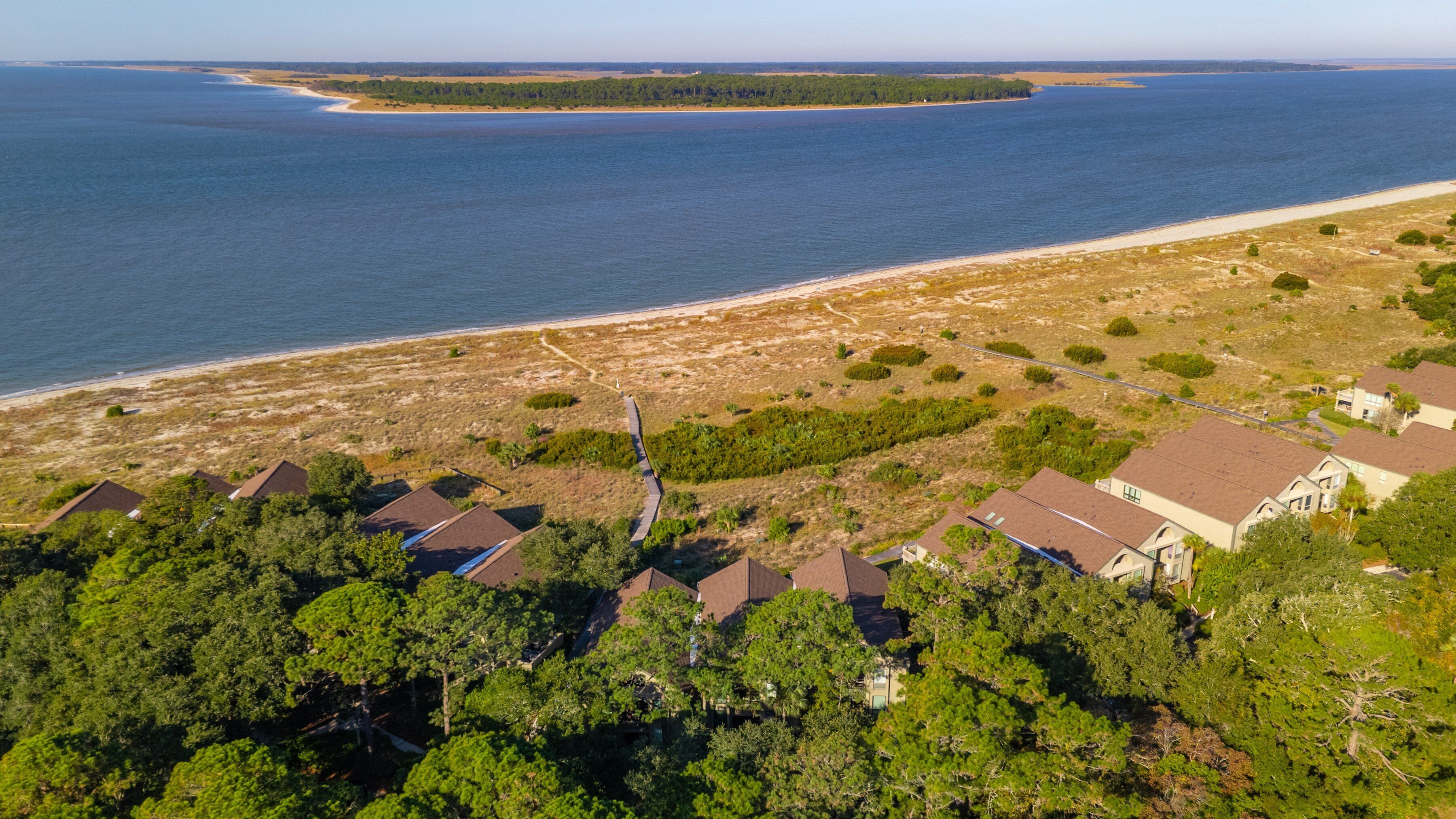 An aerial view of a coastal residential area with houses, a beach, and a forested peninsula.