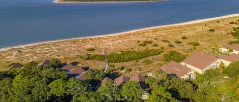 An aerial view of a coastal residential area with houses, a beach, and a forested peninsula.