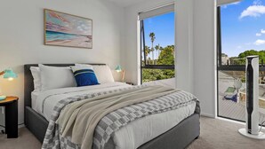 A modern bedroom with a large bed, a view of the outdoors through a balcony, and a painting on the wall. - Riverside Modern Abode with 2 Aircons and Parking (Auckland South)